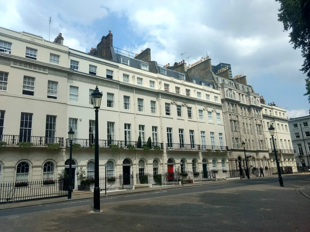 The curved cream-stuccoed Georgian terrace of Fitzroy Square in sunshine, with black railings and street lamps