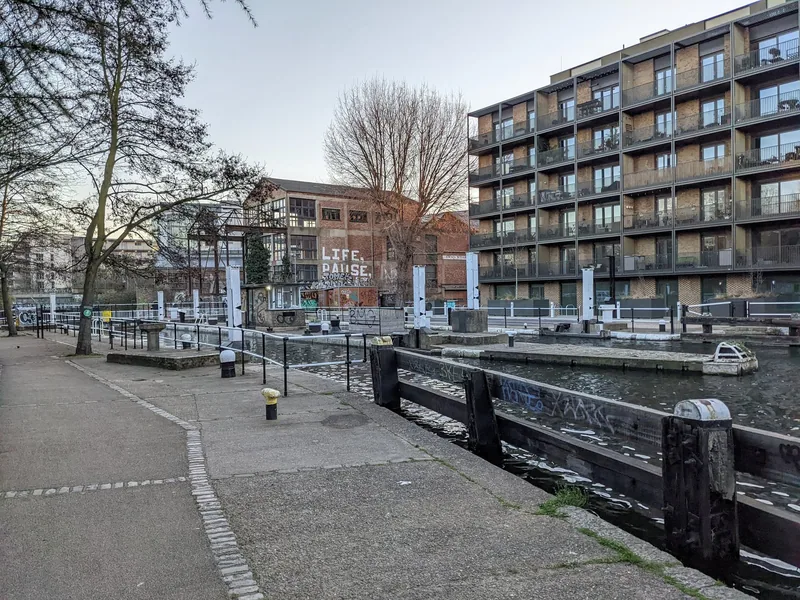 Old Ford Lock on the Lee Navigation, with the towpath, an old warehouse and new canal-side flats behind