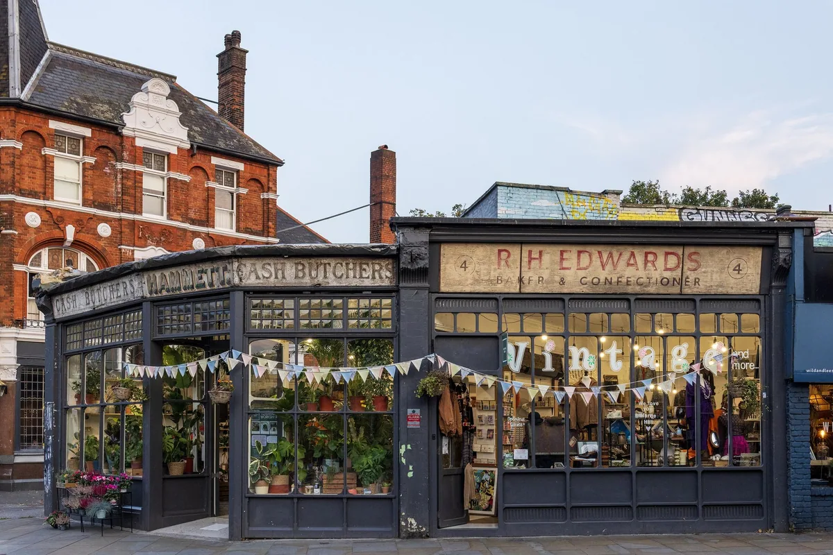 An ornate Victorian shopfront on Half Moon Lane in Herne Hill, its old gilded butcher and fishmonger signs hung with plants