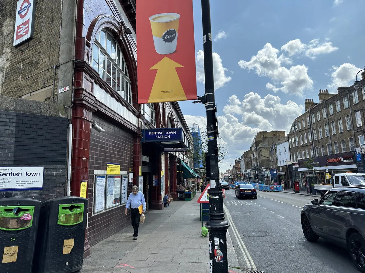 Shops and traffic along Kentish Town Road outside the Underground station entrance on a bright day