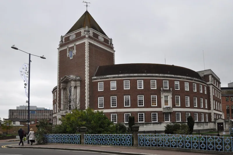 Kingston Guildhall, a curved 1930s brick building with a square clock tower, behind the blue railings of Clattern Bridge