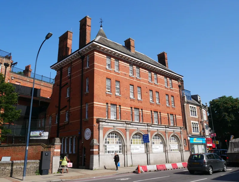 The red brick former fire station at 340 Lewisham High Street, four arched engine bays at street level under tall chimneys