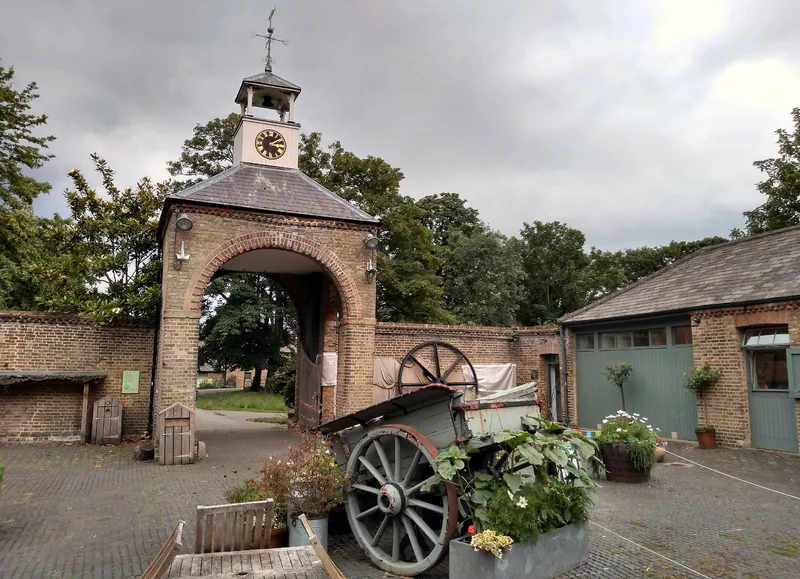 The brick archway with its clock and bell turret in the stable yard at Morden Hall Park, a planted farm cart standing on the cobbles