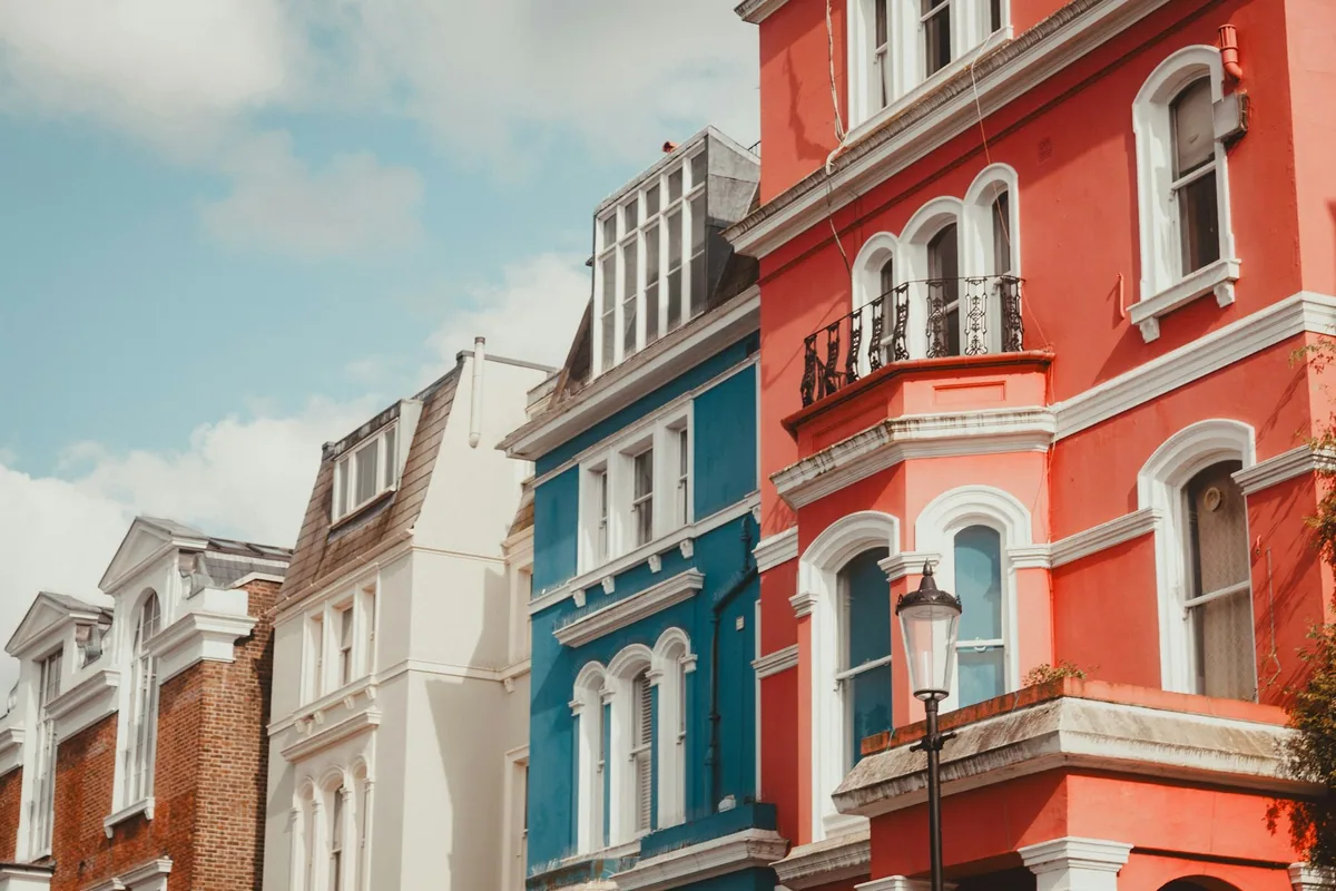 A row of brightly painted terraced houses in red, blue and cream on a Notting Hill street