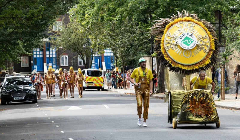 Performers in yellow costumes pushing a decorated float along the street at Notting Hill Carnival