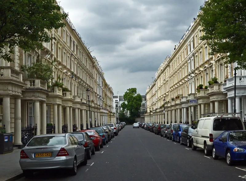 A long Pimlico street lined with white stuccoed terraced houses and parked cars under a cloudy sky