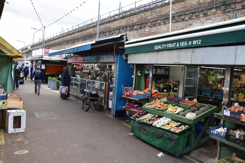 Fruit and vegetable stall in the aisle of Shepherd's Bush Market under a railway viaduct