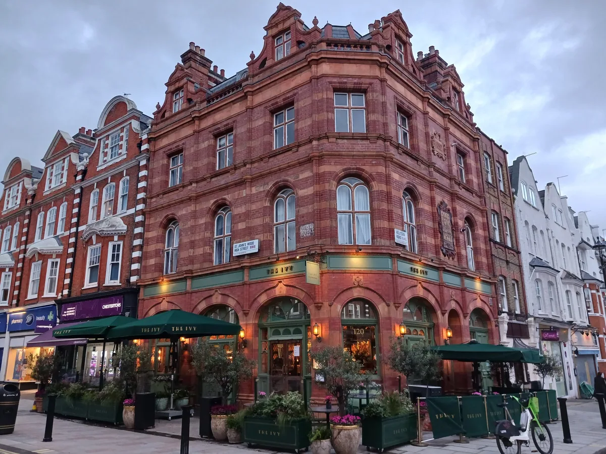 A red brick corner building with shops and awnings where St John's Wood High Street meets Allitsen Road