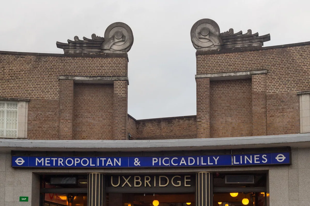 The brick front of Uxbridge tube station, winged-wheel sculptures on the parapet and a blue Metropolitan and Piccadilly Lines sign