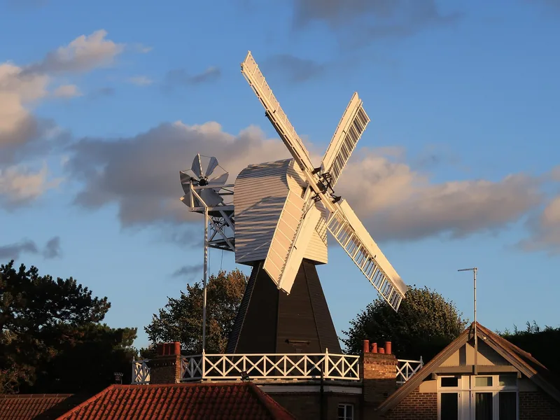 The timber tower and pale sails of Wimbledon Windmill rising above rooftops against a blue sky