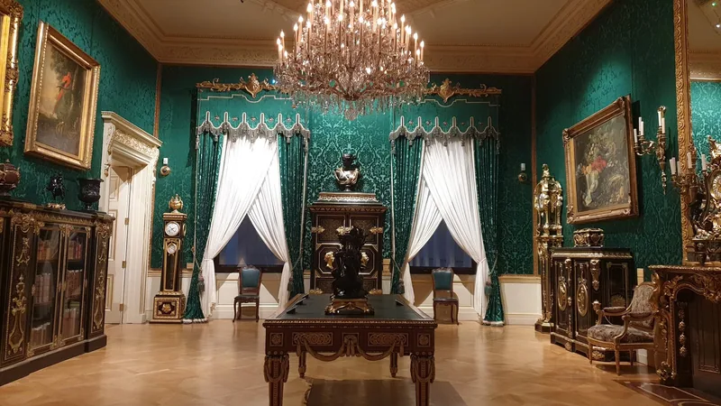 A quiet green-walled museum room with a chandelier, gilt furniture and no visitors