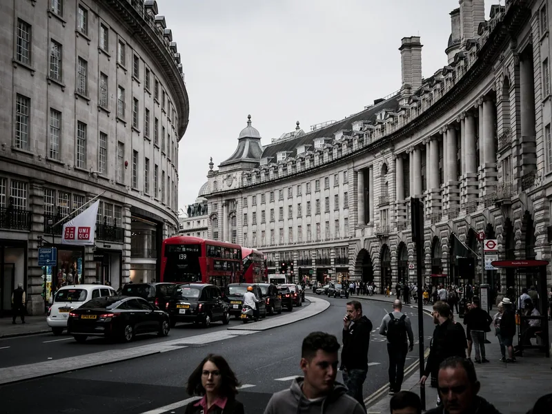Red buses and black cabs on the curve of Regent Street with people walking along the pavement