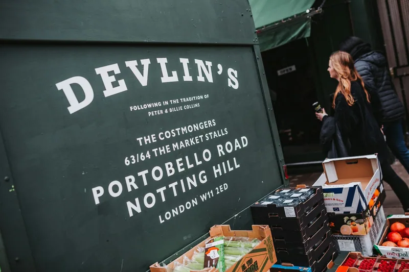 A greengrocer's painted stall board on Portobello Road in Notting Hill, with crates of fruit and veg