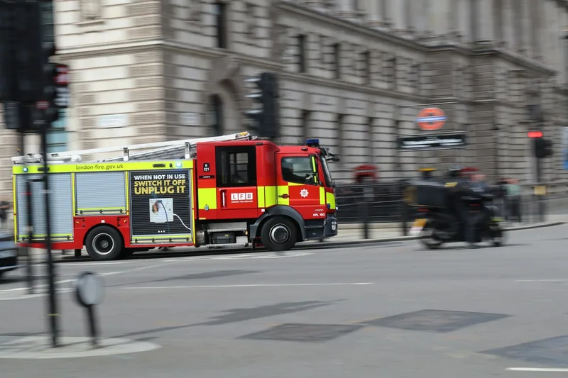 Red London Fire Brigade engine driving past stone buildings in central London