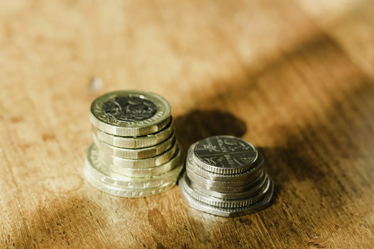 Two small stacks of British one-pound coins and twenty-pence pieces on a sunlit wooden table