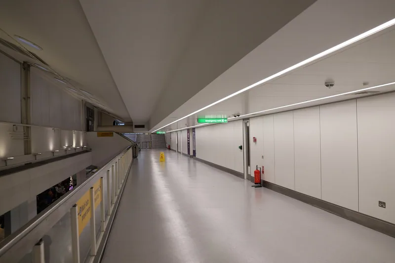A deserted upper walkway inside a Heathrow terminal, lit by a strip light running the length of the curved ceiling