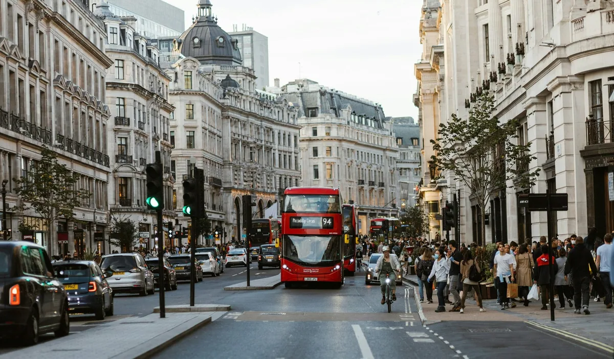 Busy central London shopping street in daytime, with pedestrians on the pavements and a red double-decker bus