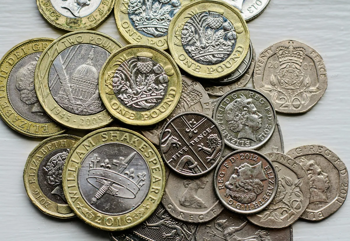 A handful of British coins - two pound, one pound, twenty pence and five pence pieces - spread on a pale table