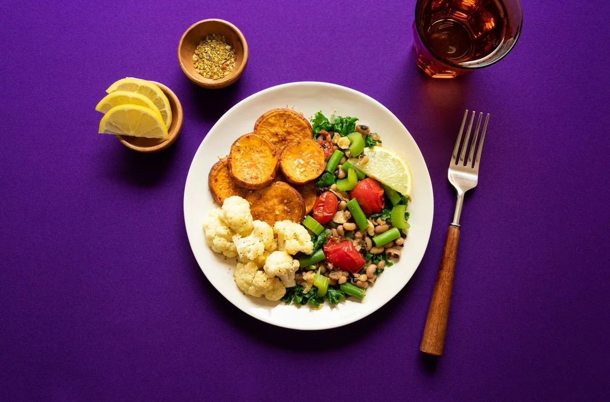 A plant-based plate of roast sweet potato, cauliflower, kale, celery and black-eyed beans with a lemon wedge
