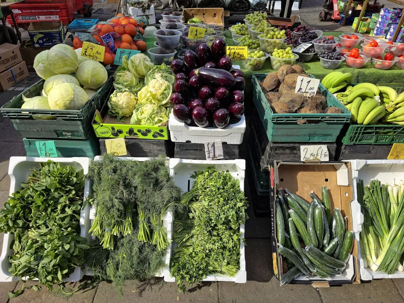 Fruit and vegetable stall at an outdoor London market, with herbs, aubergines, cabbages and cucumbers priced in pounds