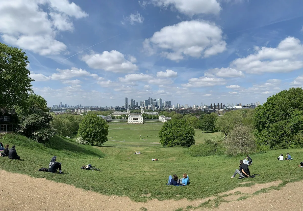 View from the grass in Greenwich Park over the Old Royal Naval College to the towers of Canary Wharf on a bright summer day