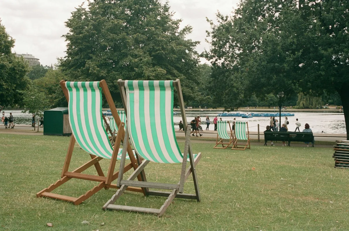 Green-and-white striped deckchairs set out on the grass of a London park, with a boating lake and pedalos behind them