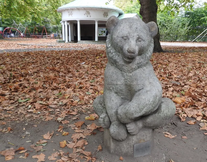 A stone bear sculpture sitting on a plinth among fallen leaves at Coram's Fields