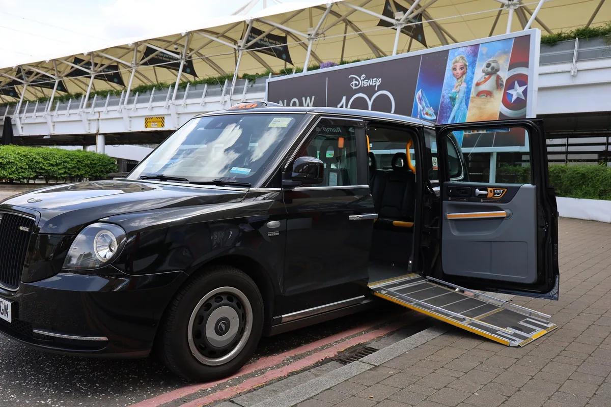 A black London taxi at the kerb with its rear door open and the wheelchair ramp folded down onto the pavement