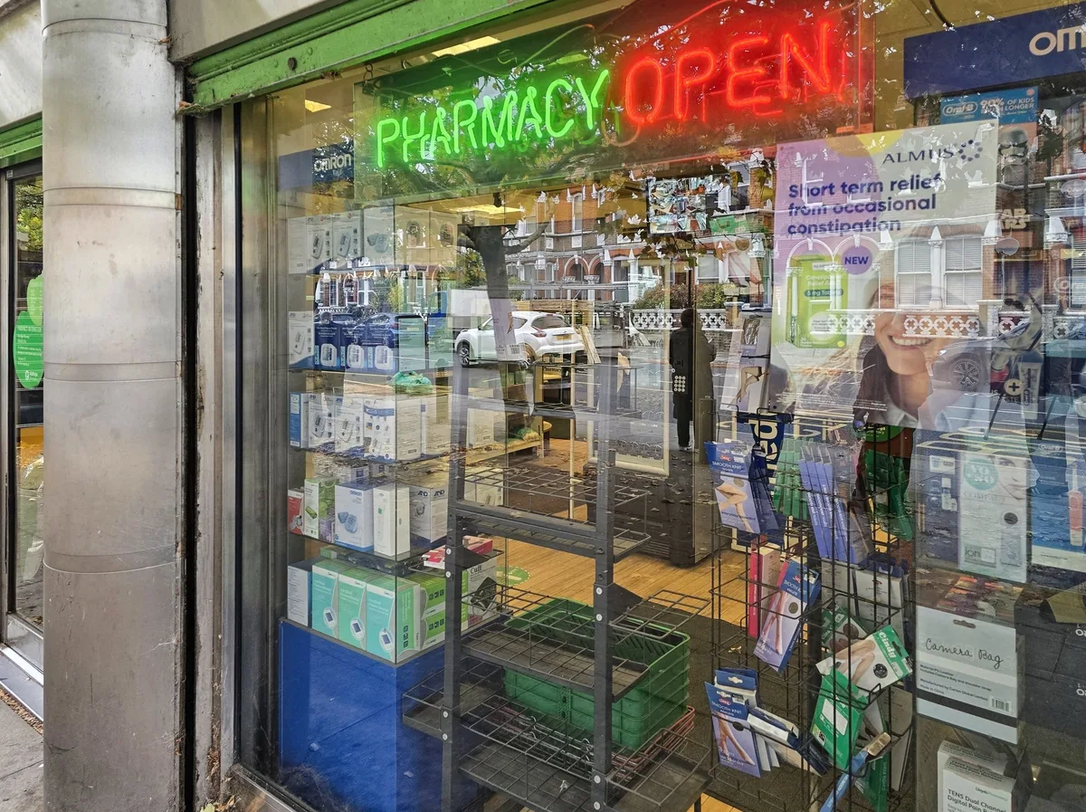 Neon PHARMACY OPEN sign in the window of a London high-street chemist