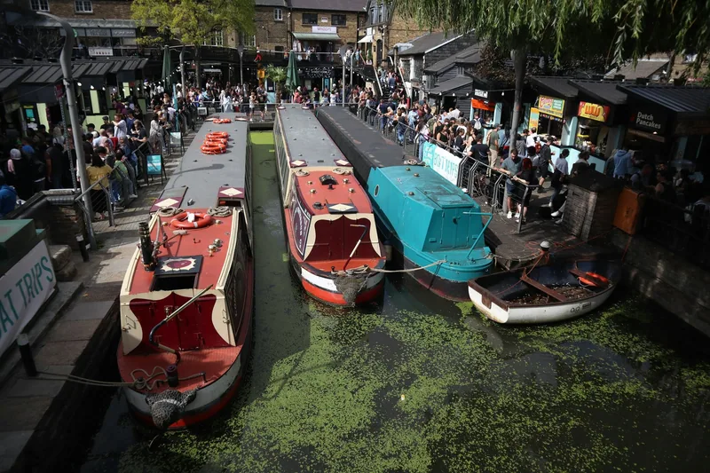 Narrowboats moored on the canal in Camden Town with crowds on the market terraces above