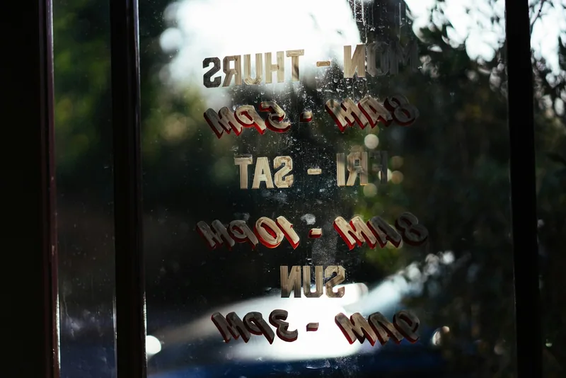 Opening hours lettered on a shop door, read from inside, listing separate Monday to Thursday, Friday to Saturday and Sunday times