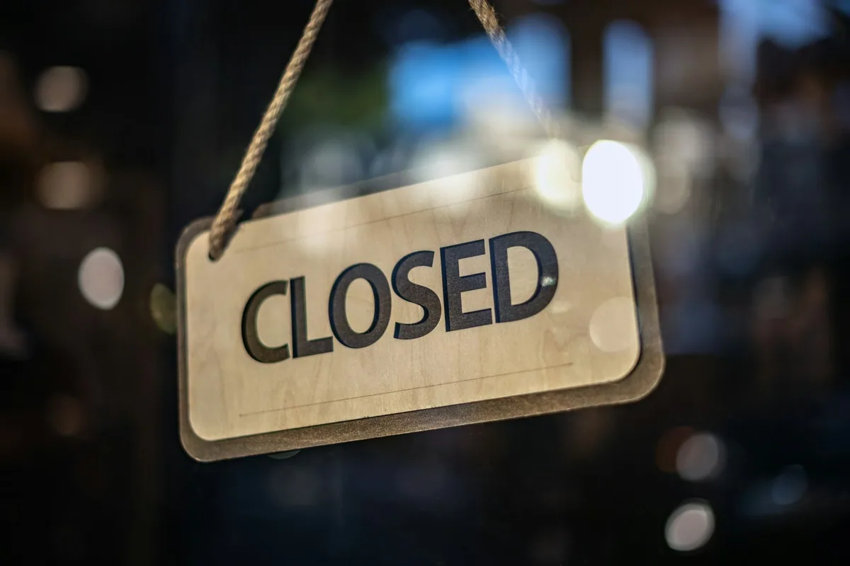 A hanging Closed sign on the glass door of a shop, with street lights blurred behind it