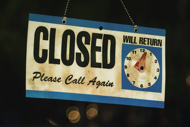 A shop door sign reading Closed, will return, with a small clock dial showing the time