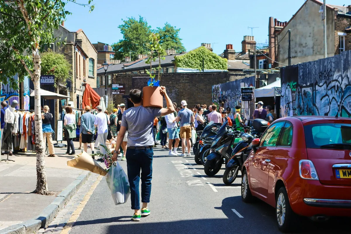 A shopper carries a potted tree and wrapped flowers away from the busy Columbia Road flower market in east London