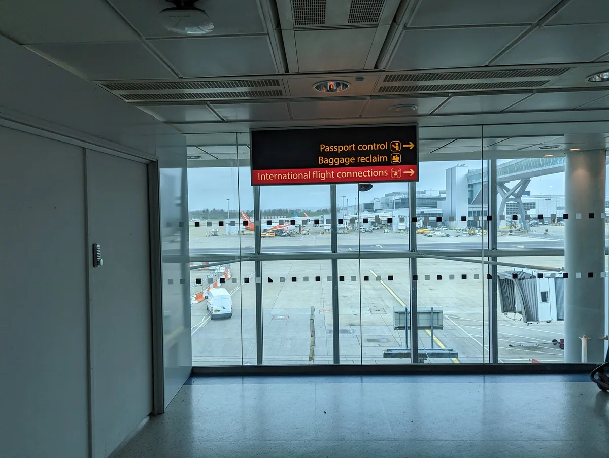 Airport signs pointing to passport control and baggage reclaim above a window onto the apron