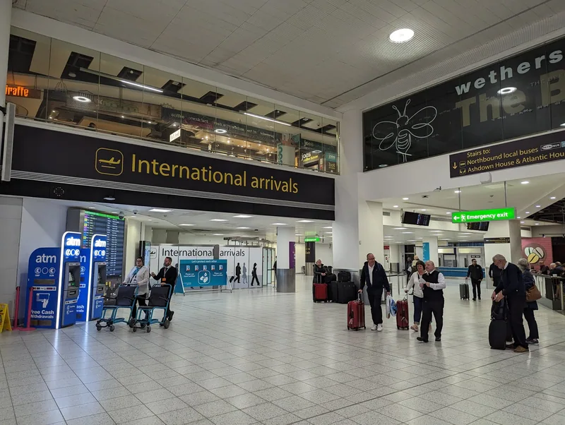 International arrivals hall at a London airport with passengers wheeling suitcases