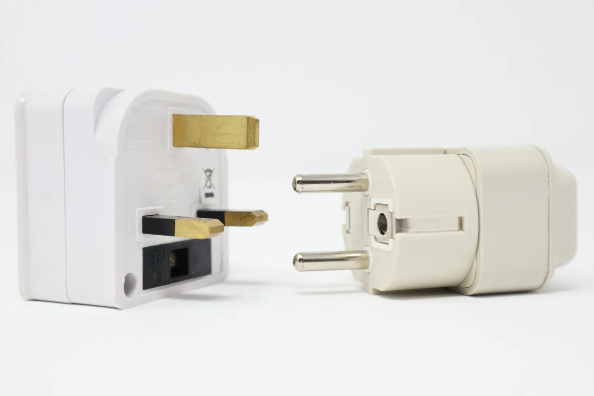 A British three-pin plug adapter next to a European two-pin plug on a white background
