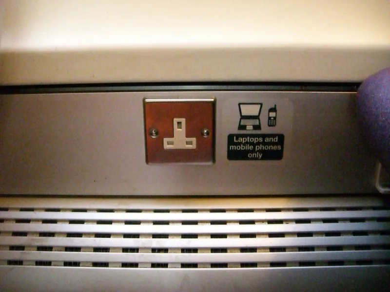 British three-pin power socket for laptops and mobile phones beside a seat on a UK train