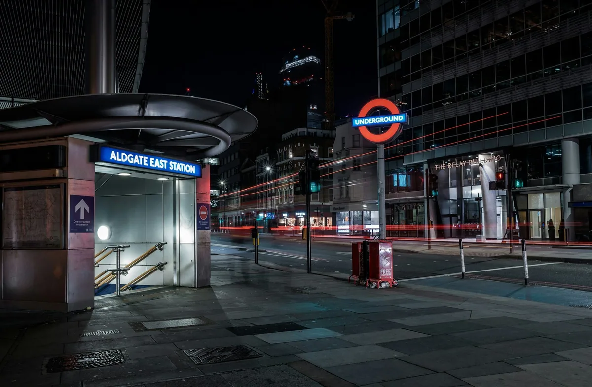 The entrance to Aldgate East Underground station at night, with an empty street and an Underground roundel beyond