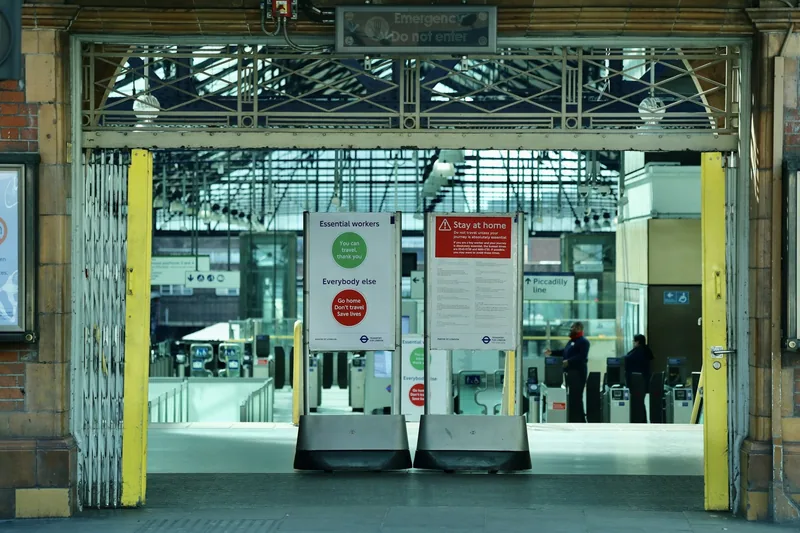 A concertina gate half drawn across a station concourse entrance, with notices about restricted travel
