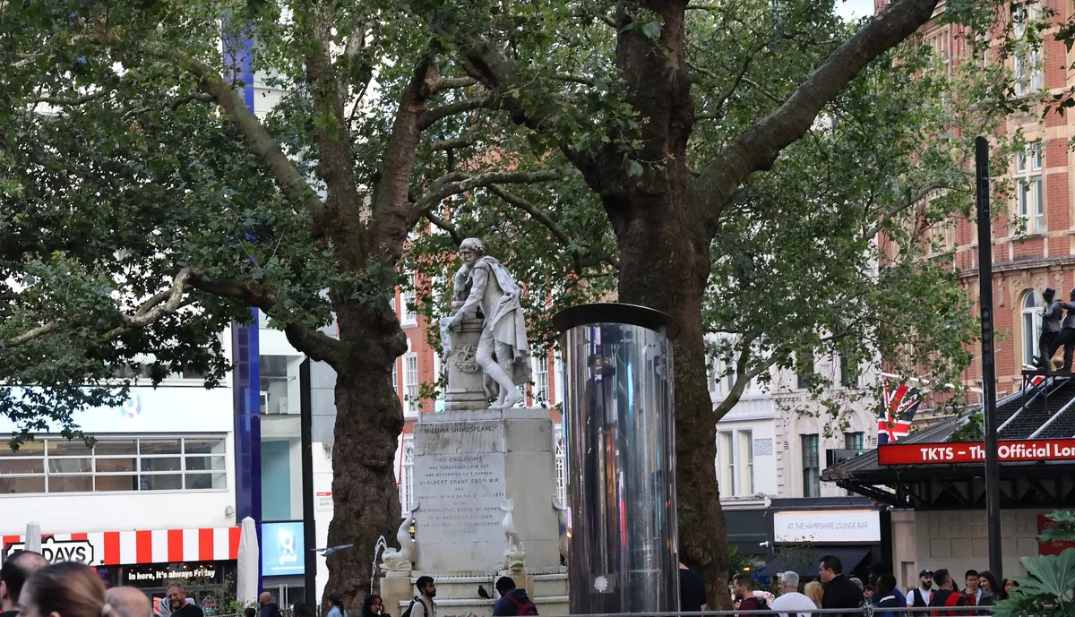 Shakespeare statue in Leicester Square gardens with the TKTS ticket booth behind the plane trees