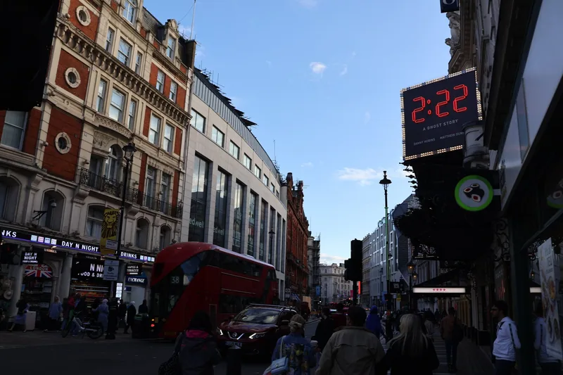 A lit theatre sign on Shaftesbury Avenue with a red double-decker bus in the street below