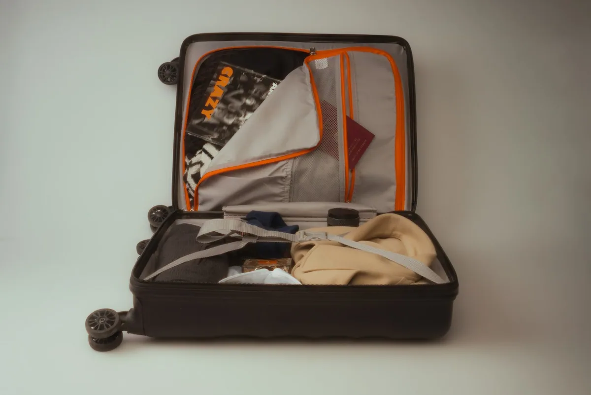 An open black suitcase on the floor, packed with folded clothes, shoes and travel essentials