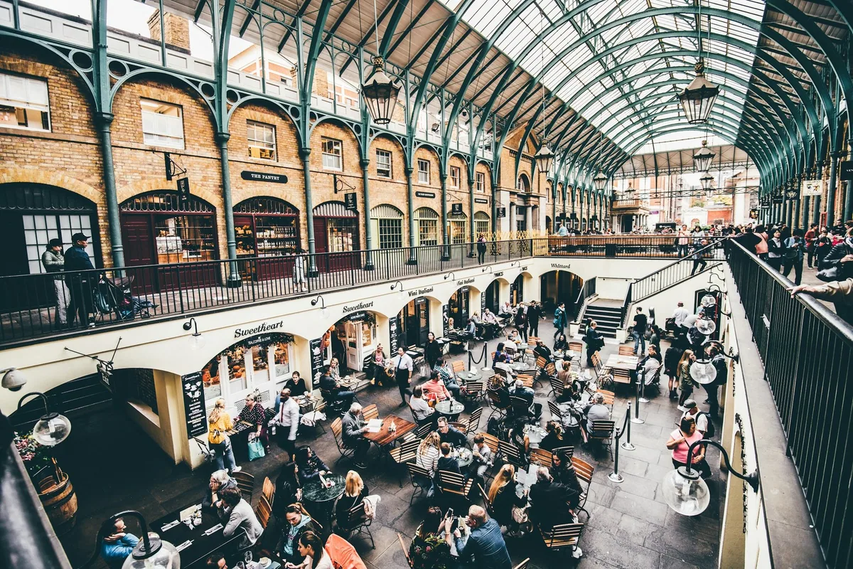 Shoppers and diners in the glass-roofed Covent Garden Market building seen from the upper gallery