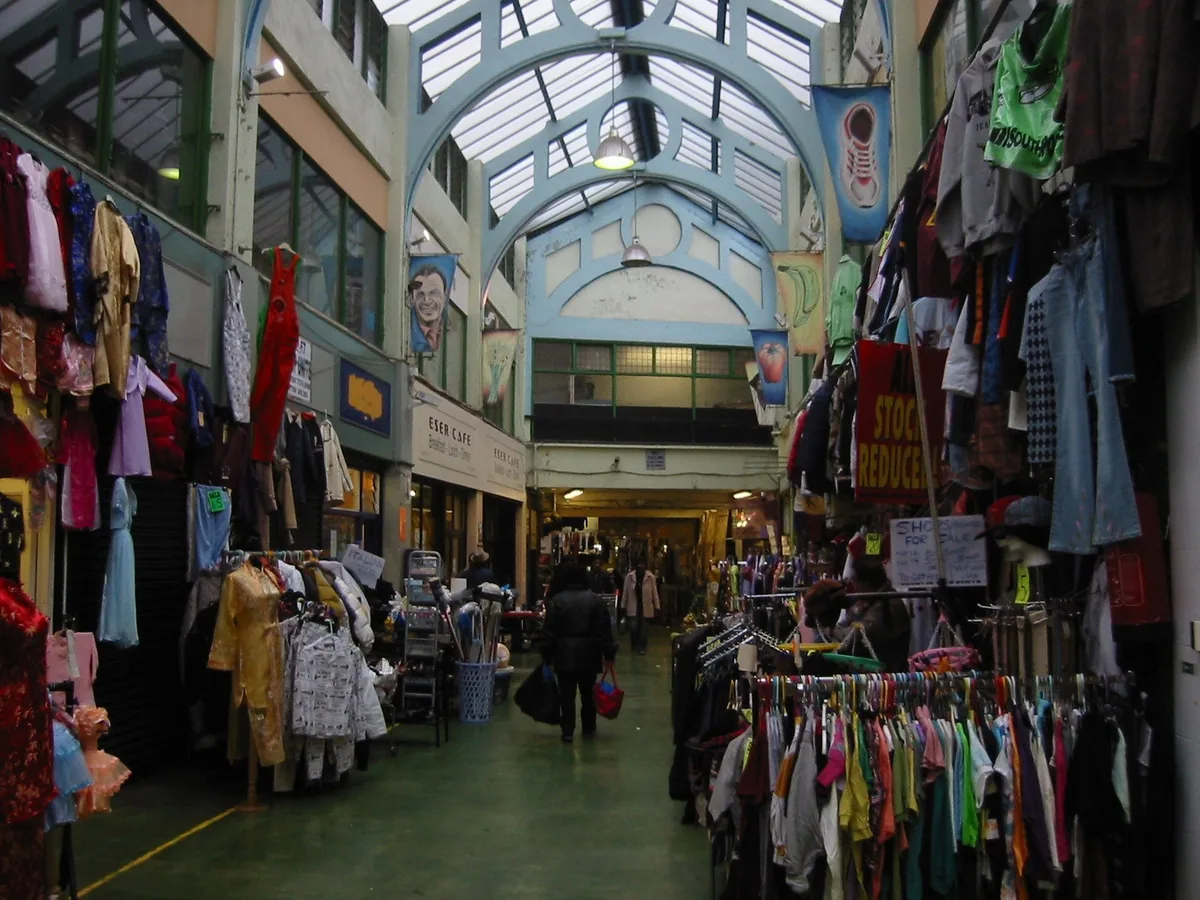 Shoppers between clothing stalls under the glazed arched roof of Brixton's covered market arcade