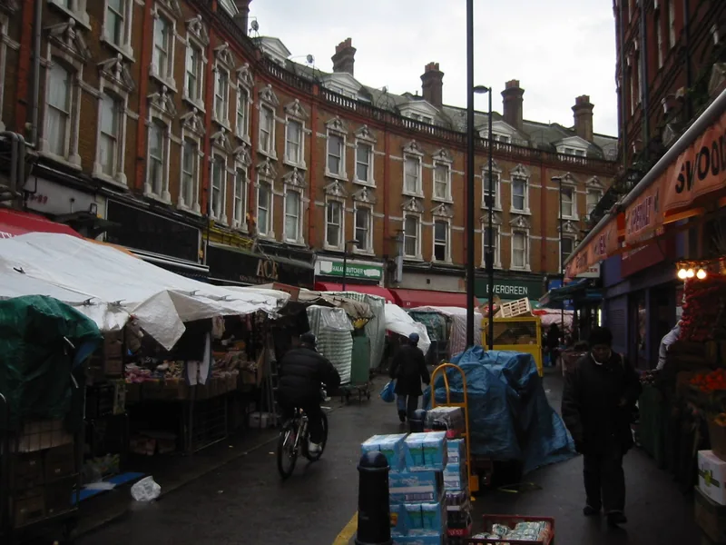 Market stalls under tarpaulins along Electric Avenue, below Brixton's curved Victorian terrace