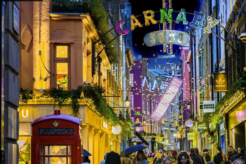 Carnaby Street after dark, strung with bright hanging decorations above the crowds and a red phone box
