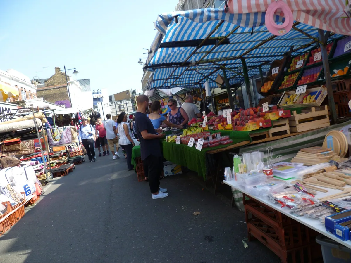 Fruit and vegetable stalls under striped awnings along Chapel Market, with shoppers in the street
