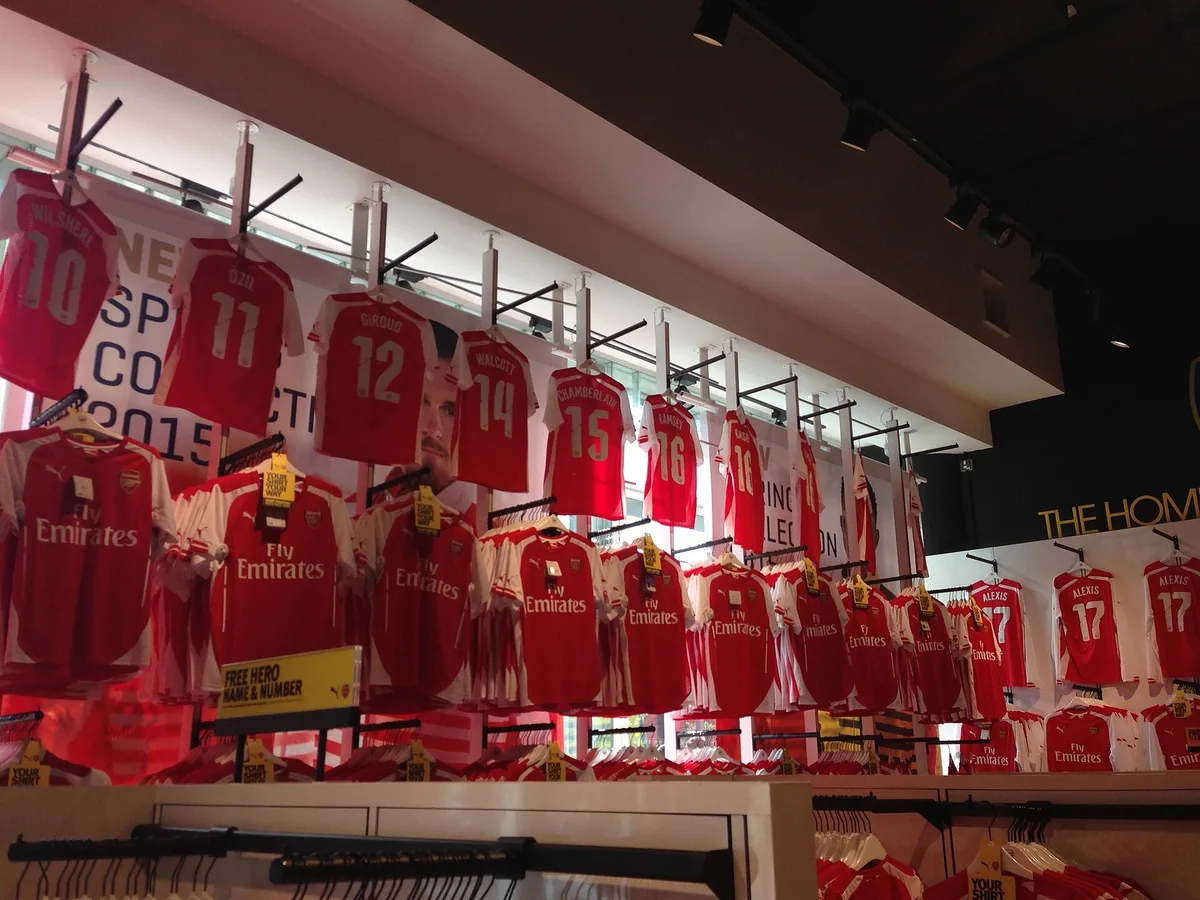 Rails of red-and-white replica football shirts with printed names and numbers, hanging with price tags in a club shop