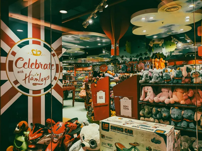Inside a Hamleys store, shelves stacked with soft toys beside a Union Jack wall sign